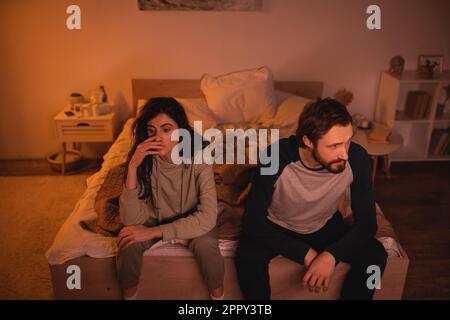 Donna insoddisfatta seduta vicino al ragazzo a letto di notte, immagine stock Foto Stock