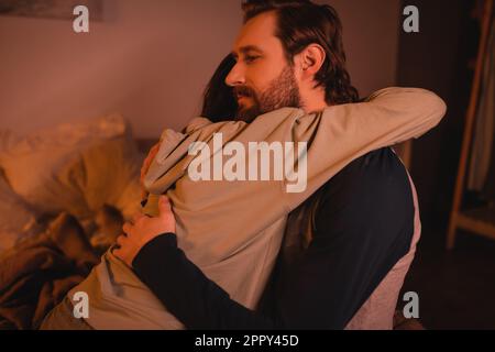 Uomo bearded abbracciando e calmando giù ragazza in camera da letto di notte, immagine di scorta Foto Stock