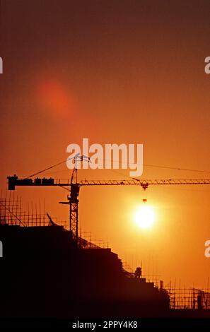 Cina. Hong Kong. Tramonto. Silhouette di gru alta sopra l'edificio in costruzione. Foto Stock