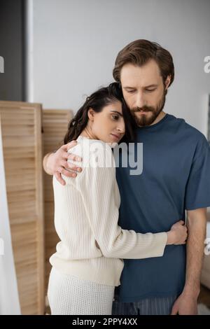 Triste coppia in pajama abbracciando a casa al mattino, immagine stock Foto Stock