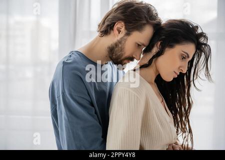 Vista laterale di un uomo trista bearded che abbraccia la ragazza a casa, immagine stock Foto Stock