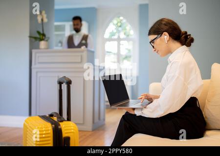 Donna d'affari che usa il laptop che indossa gli auricolari che lavorano online in hotel Foto Stock