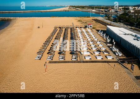 Vista aerea del drone di file di ombrelloni di paglia e lettini sulla spiaggia di Vilamoura, Algarve, Portogallo Foto Stock