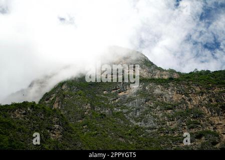 Un maestoso paesaggio montano caratterizzato da un'imponente cima montuosa avvolta da fitte nuvole grigie Foto Stock