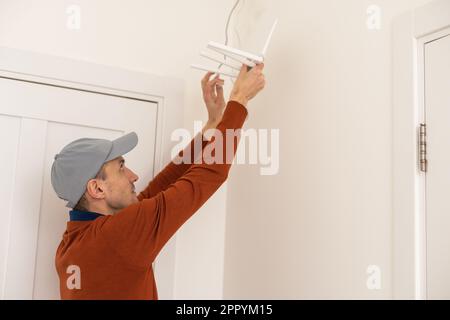 Un lavoratore installa un router sulla parete per trasmettere il segnale Internet in uffici e case, vista laterale Foto Stock