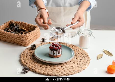 Una ragazza in un grembiule in cucina spruzza lo zucchero su un cupcake. La casalinga sta preparando un cupcake. Cottura in cucina. Foto Stock