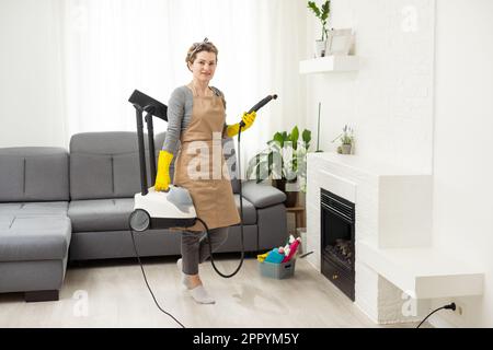 servizio di pulizia professionale. donna in uniforme e guanti spugna lava le finestre panoramiche nel cottage. lavaggio bagno turco e raschietto Foto Stock