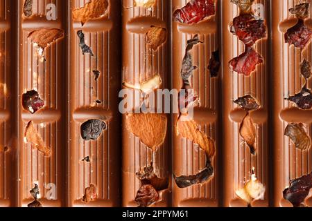 Sfondo cioccolato. Cioccolato al latte con mandorle, uva passa, bacche secche primo piano come sfondo. Foto Stock