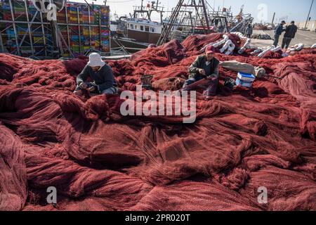 Pescatori che riparano reti da pesca nel porto di Essaouira. Foto Stock