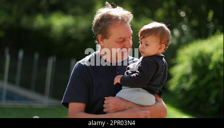 Grand-padre che tiene il bambino nelle braccia fuori nel cortile. Grand genitore legame con Grand-bambino Foto Stock