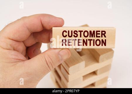 Concetto aziendale. Un uomo tiene nelle sue mani un blocco di legno con l'iscrizione - Customer Retention Foto Stock