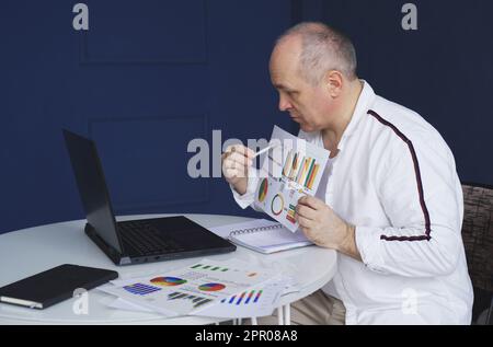 Un uomo effettua una videochiamata online, seduto a casa e parlando con una webcam del laptop, mostrando un documento. Foto Stock