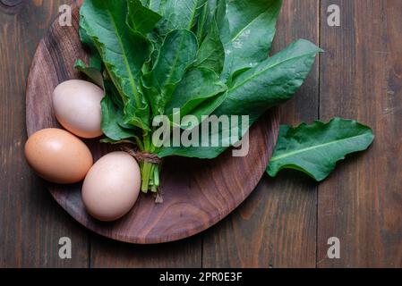 Sorgo biologico fresco, mazzo di piante di spinaci su tavolo di legno per minestra di verdure verdi primaverili e insalata. Foglie di sorgo crudo vista dall'alto dorso di verdure verdi Foto Stock