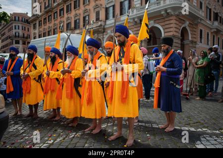 Uomini Sikh con il kirpan, scortano il Granth Sahib durante la processione per il Vaisakhi Nagar Kirtan nel distretto di Esquiline. Nei giardini di Piazza Vittorio, i Sikh di Roma cantavano canzoni di Shabad (inni divini), pregavano e rinviavano omaggio al Granth Sahib, il libro sacro. Con il Nagar Kirtan, che i Sikh di tutto il mondo fanno nel mese di Vaisaki (verso aprile), attraversando le strade del quartiere, cantando inni sacri, portarono il messaggio di Dio ad altre comunità. A Pessina Cremonese sorge il secondo tempio Sikh più grande d'Europa. Una delle unità Sikh del V britannico Foto Stock