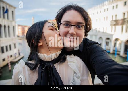 La ragazza bacia il suo ragazzo sulla guancia mentre è in vacanza a Venezia sul ponte di Rialto Foto Stock