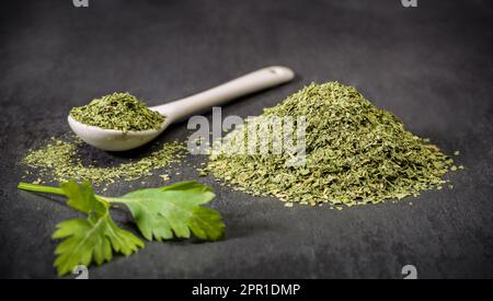 Spezie per ricette. Prezzemolo. Un cucchiaio e un mucchio di spezie di prezzemolo essiccate macinate. Ingredienti della ricetta. Foto Stock