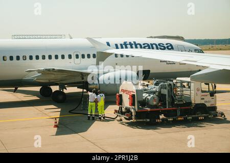 Germania - 6 luglio 2015: Un Boeing Lufthansa 737-MSN25149 arriva in un aeroporto, circondato da lavoratori in equipaggiamento protettivo che rifornisce il jet con kerosene per la sua prossima partenza. Foto Stock