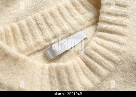 Etichetta di abbigliamento vuota su maglione in cashmere bianco, vista dall'alto Foto Stock