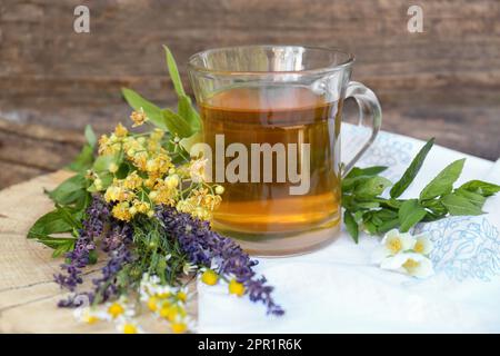 Tazza di tè aromatico caldo e diverse erbe fresche su sfondo di legno Foto Stock