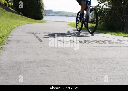 Silhouette di ciclisti sfocati in movimento su un percorso condiviso con la superficie di accesso "Share with Care" intorno alla riva del lago Taupo. Foto Stock