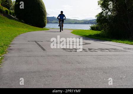 Silhouette di ciclisti sfocati in movimento su un percorso condiviso con la superficie di accesso "Share with Care" intorno alla riva del lago Taupo. Foto Stock