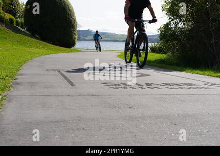 Silhouette di ciclisti sfocati in movimento su un percorso condiviso con la superficie di accesso "Share with Care" intorno alla riva del lago Taupo. Foto Stock