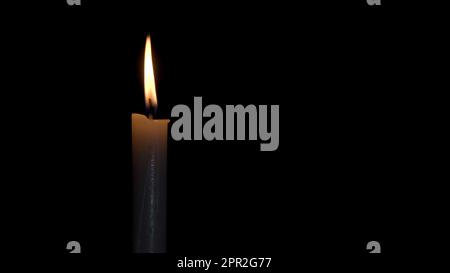 Una candela brucia con una fiamma brillante su uno sfondo nero. La fiamma di una candela di cera risplende misteriosamente nell'oscurità. Illustrazione della memoria, C Foto Stock