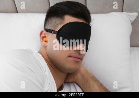 Uomo con tappi auricolari in schiuma e maschera che dorme a letto Foto Stock