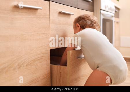 Piccolo bambino esplorando cassetto in cucina. Situazione pericolosa Foto Stock