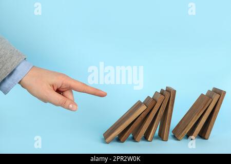 Donna che causa la reazione a catena spingendo la tessera domino su sfondo azzurro, primo piano Foto Stock