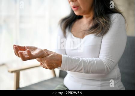 Immagine ravvicinata di una donna matura asiatica infelice che soffre di dolore alle articolazioni del polso, sfregando il polso. Foto Stock