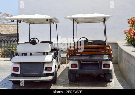 Le auto da golf elettriche bianche sono parcheggiate in piccoli veicoli elettrici con le tende dal sole in un paese caldo tropicale esotico resort di villeggiatura del sud. Foto Stock