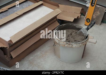 Mix adesivo, livella a bolla e piastrelle in ceramica sul pavimento interno Foto Stock