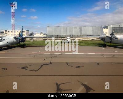 Tre grandi aerei bianchi potenti veloci con turbine, ali e viti sono parcheggiati vicino agli hangar degli aerei sulla pista. Foto Stock