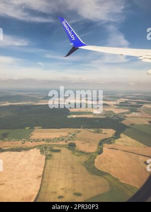 l'aereo vola ad una grande altezza su un campo vuoto con erbe e verde. la coda del piano è visibile nella finestra. trasporto aereo. Foto Stock