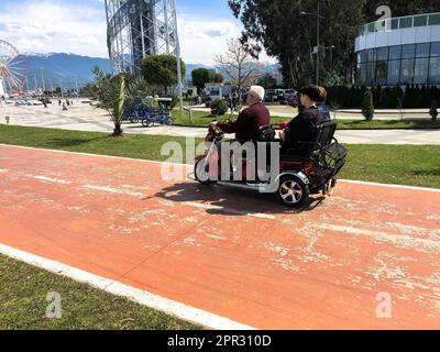 La gente viaggia in una piccola auto elettrica, una golf car sul lungomare su una spiaggia di sabbia contro le palme verdi tropicali del cielo blu. Georgia, Batum Foto Stock