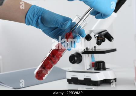 Scienziato che preleva la carne coltivata grezza dalla provetta con pinzette in laboratorio, primo piano Foto Stock