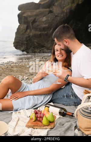 Felice giovane coppia che ha pic-nic sulla spiaggia vicino al mare Foto Stock