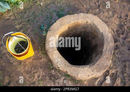 Acqua bene in un giardino tipico dell'Africa occidentale con un secchio giallo Foto Stock