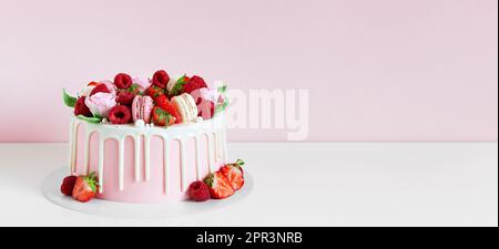 Panorama di dolce di compleanno con bacche, macaron e decorazioni floreali sul tavolo. Bella torta rosa decorata con macaron, lamponi, fragole Foto Stock