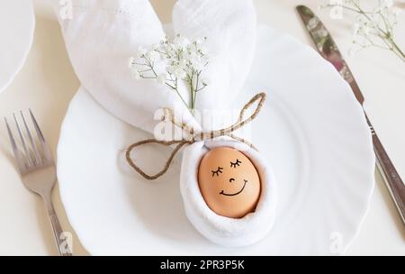 Uovo di Pasqua con un viso carino in un piatto con orecchie conigliate, come felice concetto di Pasqua. Uovo di Pasqua con occhi assondati in luce solare. Buon concetto di Pasqua. Foto Stock