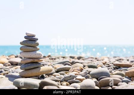 Primo piano di una pila di pietre in perfetto equilibrio su una bella spiaggia soleggiata. Piramide di pietre marine sulla riva del mare a spiaggia di ciottoli. Foto Stock