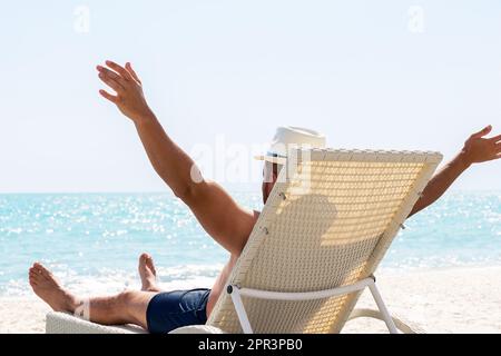 Giovane uomo in cappello bianco che si rilassa in sedia a sdraio sulla bellissima spiaggia di sabbia. Concetto di vacanza estiva. Uomo che si rilassa sulla spiaggia, vista sull'oceano, Republique Dominicana Foto Stock