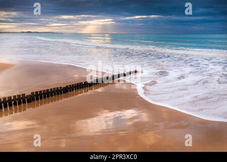 Vista aerea di un'alba su una spiaggia di sabbia con onde bianche intorno a un groyne di legno a Torquay sulla Great Ocean Road a Victoria, Australia Foto Stock