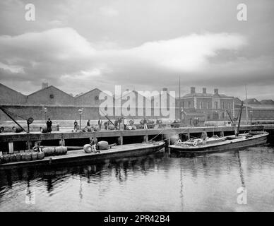 Una vista di fine 19th ° secolo dei lavoratori che caricano barili Guinness su chiatte ormeggiate alle banchine sul fiume Liffey, Dublino, Irlanda. Quando St. James's Gate Land è stato affittato a Arthur Guinness a $ £45 all'anno per 9.000 anni, la fabbrica di birra fondata nel 1759 è stata la casa di Guinness da allora. È diventata la più grande birreria d'Irlanda nel 1838 e la più grande al mondo entro il 1886, con una produzione annua di 1,2 milioni di barili. Foto Stock