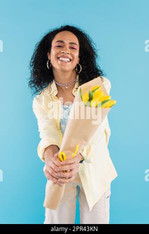 donna afro-americana overjoyed che tiene bouquet di tulipani gialli in mani distese isolato su blu, immagine di scorta Foto Stock