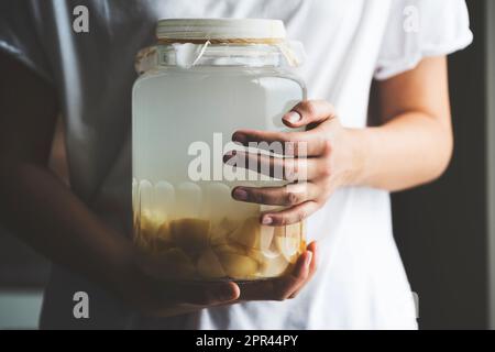 Donna che tiene aceto di sidro di mela in vaso coperto di cheesecloth Foto Stock