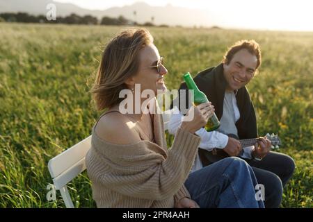 Ora legale. Bella giovane coppia godendo del tempo in campo intorno all'erba. Stile di vita, amore, datazione, concetto di vacanza. Privato. Donna che beve birra, uomo Foto Stock