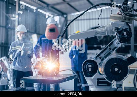 Il controllo del lavoro del team di ingegneri aziona un piccolo braccio di saldatura robot in un'officina di metallo Foto Stock