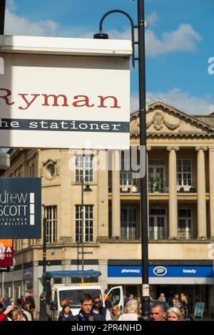 Collezione di cartelli per Shopfront che includono per Ryman lo Stationer in una fila di punti vendita al dettaglio / cartello per negozi sulla facciata anteriore del negozio / entrata per negozi al dettaglio nella trafficata zona commerciale del centro cittadino. Cheltenham Spa. Gloucestershire. REGNO UNITO. (134) Foto Stock